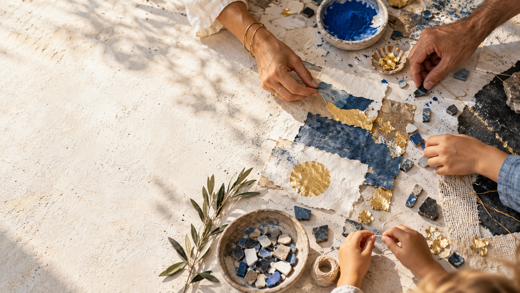 Mani di adulti e bambini che creano insieme con carta, pigmenti, mosaico e foglia d’oro